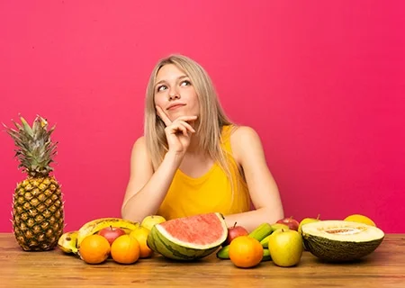 Mulher pensativa sentada em mesa com frutas